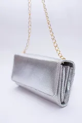 Cartera tipo sobre color beige con textura granulada y correa de cadena dorada.