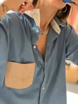 Camisa de corte oversize color celeste, confeccionada en una combinación de lino, lienzo y pana. Presenta cuello clásico, cierre frontal con botones y un bolsillo de parche en color beige en el pecho.