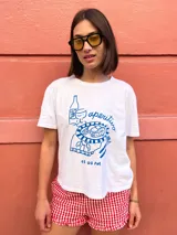 Remera blanca de corte holgado con estampa frontal en color azul que ilustra una escena de aperitivo con botella, copa y plato, acompañada por la palabra 'aperitivo' y la hora '13:00 PM'.