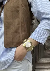 Brazalete rígido de metal dorado con tres incrustaciones ovaladas de nácar, diseño ajustable.