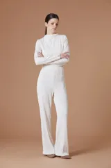 Blusa de manga larga con cuello alto y textura plisada con ondas verticales. Presenta un corte cropped y detalles de botones dorados en los puños.