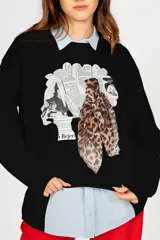 Sweater negro con cuello redondo y mangas largas. Presenta un estampado con diseño de collage de recortes de diario y una bufanda de animal print.