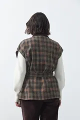 Chaleco de corte relajado con estampado a cuadros en tonos tierra, cuello camisero oscuro y cierre frontal con botones. Incluye un cinturón de la misma tela para ajustar a la cintura y bolsillos frontales.