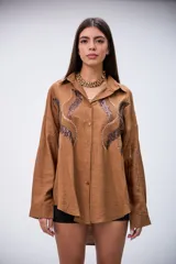 Camisa marrón de manga larga con detalles de lentejuelas y bordados en el frente. Tiene cuello clásico y botones frontales.