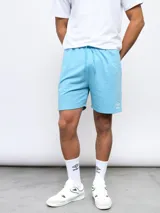 Bermuda de felpa color celeste, con cintura elástica y cordón de ajuste. Presenta el logo Umbro bordado en la pierna izquierda.