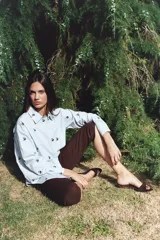 Camisa negra de algodón con bordados de pequeñas flores rosas. Presenta cuello clásico, cierre frontal con botones y mangas largas.