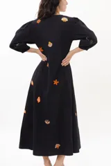 Vestido largo blanco de algodón con bordados de motivos marinos en tonos naranja, verde y azul. Tiene escote en V, mangas 3/4 abullonadas y cierre frontal con botones.