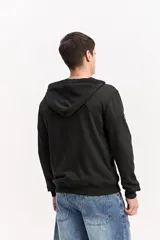 Campera de algodón gris melange con capucha, cierre frontal completo y bolsillos laterales. Cuenta con un parche rectangular negro con inscripciones en la manga y cordones ajustables para la capucha.
