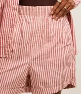 Short tipo runner de sarga color crudo con rayas verticales rojas, cintura elástica y ruedo doblado.