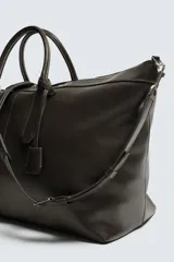 Bolso shopper de cuero vacuno con acabado abatanado, diseño minimalista con cierre de cremallera superior, doble asa de mano y detalle de llavero colgante. El interior incluye un bolsillo plano y un bolsillo con cierre.