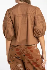 Blusa de algodón color marrón con cuello en V, mangas tres cuartos con puños elásticos y detalles de encaje y alforzas en el frente.