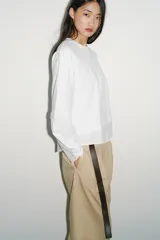 Camiseta oversize de cuello redondo y manga larga con puños abotonados. Confeccionada en algodón, presenta un diseño con combinación de tejidos a tono y bajo asimétrico.