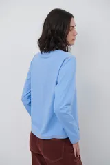 Remera de manga larga color marrón, con costuras a la vista en color blanco que resaltan los cortes de la prenda. Presenta un pequeño bordado blanco en la parte inferior y un corte recto.