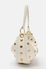 Bolso de hombro de diseño saca multiposición color blanco, decorado con tachas metálicas doradas y aros metálicos que conectan el cuerpo con la manija. Cuenta con cierre de cremallera metálica y bolsillo interior.