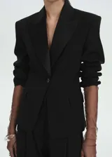 Chaqueta de corte sastre en mezcla de lana, color negro, con solapas satinadas, cierre frontal de un botón y bolsillos con solapa. Presenta mangas largas con detalle de tejido semitransparente en los puños.