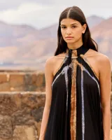 Vestido largo negro de viscosa fluida con cuello halter y espalda descubierta. Presenta un diseño vaporoso con un panel frontal y trasero con estampado difuminado en tonos tostados y azulados, y un volante fruncido en el bajo.