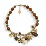 Collar corto con cuentas de madera y resina, decorado con una cadena frontal que sostiene un mix de dijes colgantes en forma de flores y figuras geométricas. Incluye cierre de mosquetón con cadena de alargue.