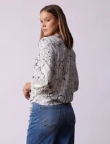 Blusa blanca estampada con flores negras, cuello redondo, abertura con botones y mangas 3/4 con frunce. Tiene terminación con nudo en el ruedo.