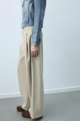 Pantalón de tiro medio con diseño de pierna ancha y pinzas frontales. Cuenta con bolsillos laterales ocultos, falsos bolsillos traseros de vivo, trabillas en la cintura y cierre frontal con cremallera y ganchos metálicos.