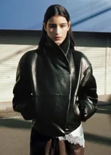 Chaqueta de estilo bomber color negro, confeccionada en 100% piel ovino con acabado de napa y diseño oversize. Cuenta con cuello alto envolvente, manga larga con puños ajustables, cierre delantero oculto con botón magnético y forro interior de poliéster.
