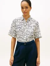 Camisa de manga corta Tommy Hilfiger de corte amplio y hombros ligeramente caídos, confeccionada en puro lino blanco con estampado geométrico de líneas azules. Cuenta con cuello inglés, cierre frontal de botones, bolsillo de parche en el pecho y logo bordado.