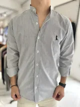 Camisa con cuello mao y diseño a rayas verticales en tonos blanco y negro, con cierre frontal de botones y detalle bordado en el pecho.