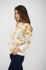 Buzo de tejido de punto con diseño estampado de flores en tonos mostaza y gris sobre fondo blanco. Presenta cuello redondo, mangas largas y corte recto.
