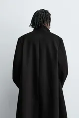 Abrigo negro de corte recto confeccionado en tejido con lana. Tiene cuello alto, manga larga con puños abotonados, bolsillos laterales y abertura en la espalda. Cierre frontal con botones.