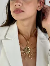 Colgante de diseño en latón dorado, compuesto por una gargantilla rígida circular y un dije central en forma de sol con líneas orgánicas. Incluye un cordón de cuero marrón ajustable con detalles metálicos.
