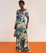 Vestido largo de viscosa con estampado tropical de flores blancas y hojas verdes y azules. Presenta escote cuadrado con lazo ajustable en el centro del busto y mangas cortas abullonadas. La falda es escalonada con volados.