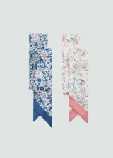 Pack de dos pañuelos estrechos y alargados de tejido fluido con diseño estampado floral. Uno presenta tonos azules y rosas con borde azul, mientras que el otro tiene un fondo claro con motivos botánicos y borde rosado.