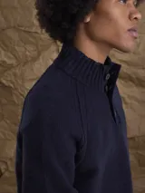 Sweater de punto en color beige, con cuello alto y cierre frontal parcial de botones. Presenta mangas largas con puños acanalados y diseño de corte clásico.