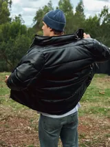 Campera puffer negra de cuero sintético con cierre frontal y cuello alto.