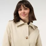 Trench midi color beige con cuello camisero, cierre frontal de botones y bolsillos laterales. Diseño clásico de gabardina con solapas y estructura fluida.