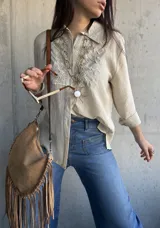 Camisa beige de manga larga con diseño bordado en el pecho, cuello camisero y cierre frontal de botones.