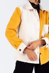 Camisa color mostaza de paño, corte oversize, con cuello clásico, cierre frontal con botones, mangas largas con puños abotonados y dos bolsillos de parche en el pecho.