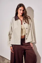 Trench corto de corte oversize con estampado de cuadros finos en tonos beige y verde. Presenta cuello camisero en contraste de color marrón oscuro, cierre frontal con botones y mangas largas con detalle de trabas en los puños.