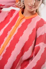 Saco de tejido de punto con rayas verticales rosas y rojas, cuello redondo y botones naranjas.
