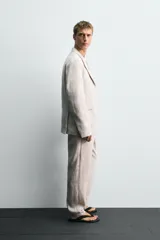 Pantalón de traje regular fit confeccionado en tejido de lino, con bolsillos laterales y bolsillos traseros de vivo con botón. Presenta cierre frontal con cremallera y botón.