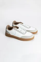 Zapatilla acordonada de diseño minimalista, con cuerpo en color blanco, detalles en gamuza gris claro y suela de goma en tono caramelo.