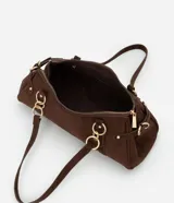 Cartera mediana de diseño alargado y estructura firme, confeccionada en gamuza sintética de color marrón. Cuenta con doble asa fina sujeta por argollas metálicas doradas, cierre superior y detalles de solapas decorativas con tachas en los laterales.