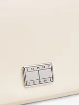 Cartera compacta Tommy Jeans de color blanco marfil con acabado liso, cierre de solapa magnética y detalle de parche metálico con logo en la parte delantera. Cuenta con una correa tejida ajustable y extraíble, compartimento principal y bolsillo interior con cremallera.