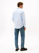Camisa de popelín de algodón celeste con sutiles rayas verticales blancas, de corte regular, manga larga y cuello camisero con botones. Presenta cierre frontal con botones y el logo bordado de Tommy Hilfiger en el pecho.