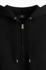 Campera canguro de felpa negra con capucha ajustable, cierre frontal completo y bolsillos tipo parche, de corte oversized.
