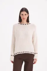 Sweater de punto grueso en color beige, con diseño de cuello redondo y detalle de pespuntes decorativos en color chocolate en el cuello, el ruedo y los puños.