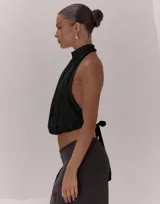 Top negro con escote halter y cuello alto. Presenta un diseño cruzado en el frente con pliegues, espalda descubierta con lazo regulable y bajo con terminación elástica.