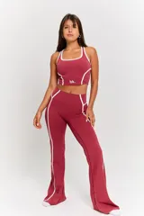Conjunto deportivo compuesto por un top corto y un pantalón largo, ambos de color bordó con detalles de líneas blancas en los costados. El top presenta cuello redondo y el logo 'bk.' estampado en el frente.