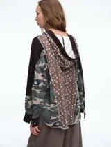 Buzo con capucha de diseño patchwork que combina paneles de tejido waffle negro, estampado camuflado y estampado floral. Presenta cierre frontal parcial con botones, bolsillo tipo parche en el pecho y mangas largas con puños.