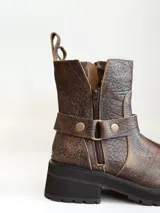 Bota corta de cuero vacuno en color chocolate con efecto desgastado. Presenta una suela track de goma negra, detalle de pulsera desmontable con tachas metálicas y cierre lateral.