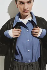 Camisa de corte oversized confeccionada en popelina de algodón con diseño de microcuadros. Presenta cuello clásico, bolsillo de parche en el pecho, cierre frontal con botones, hombros caídos y mangas largas con puños abotonados. Incluye canesú con pliegue en la espalda y bajo recto con aberturas laterales redondeadas.